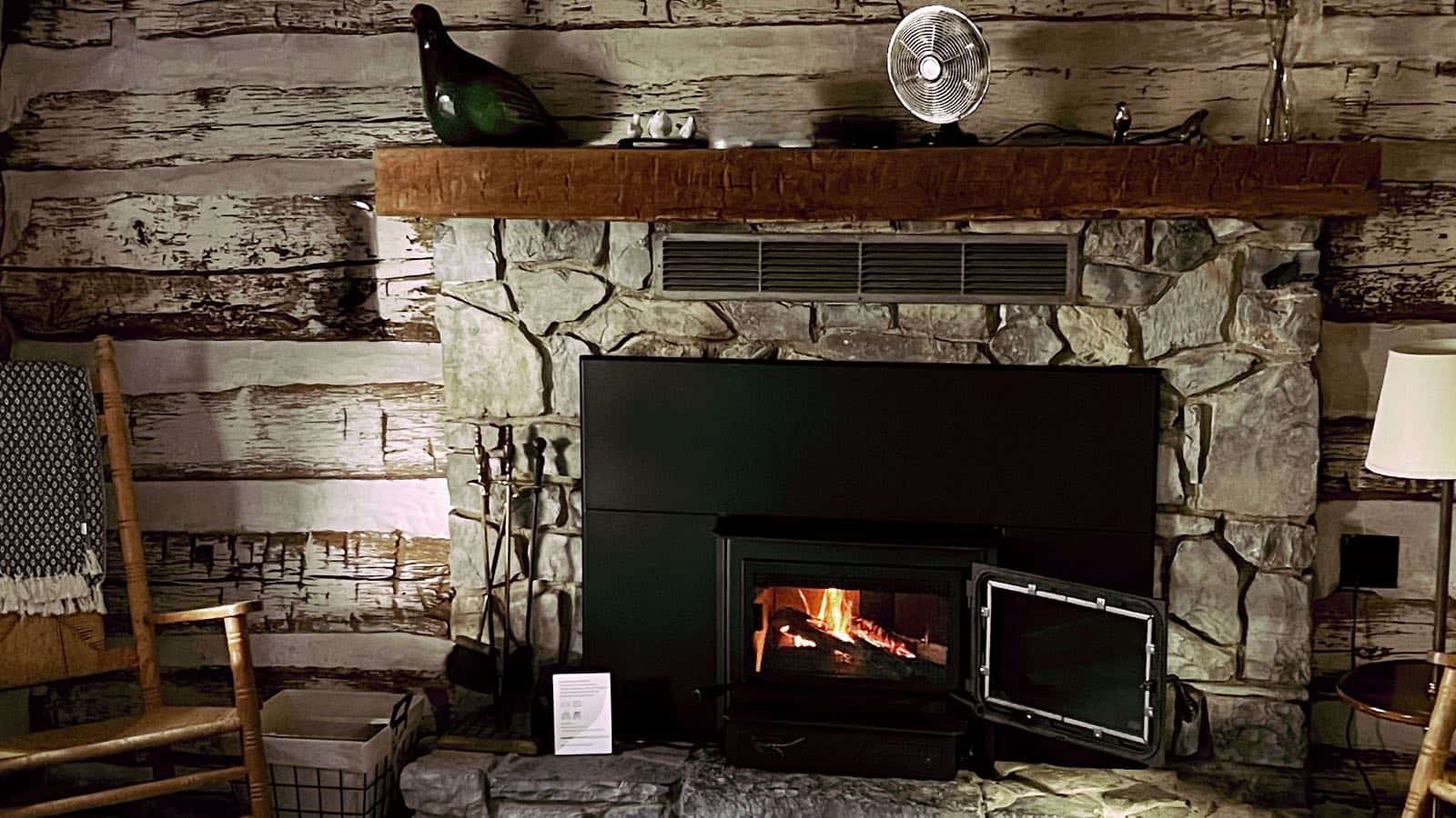 Close up view of room with aged wood paneling on the walls and stone brick fireplace with wooden mantel