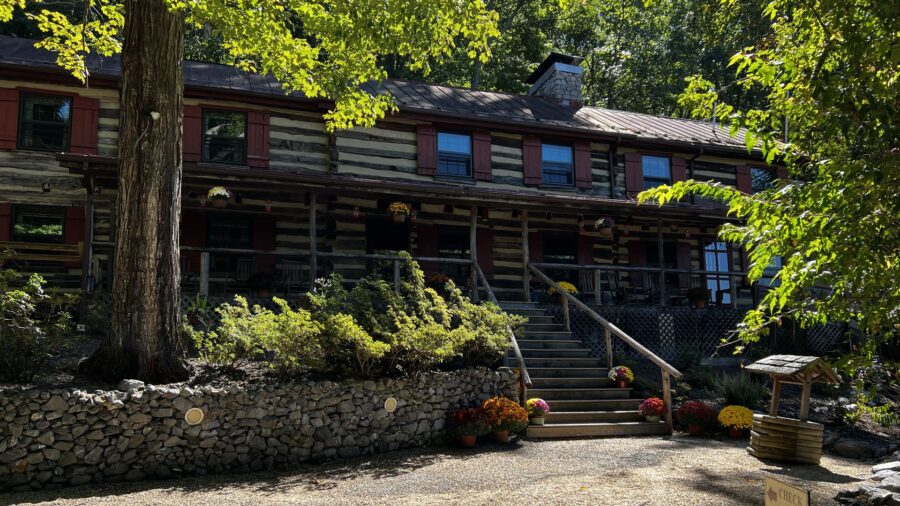 Exterior view of property which looks like a large log cabin surrounded by large green trees